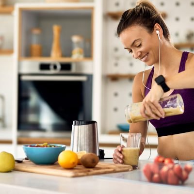 Happy sportswoman pouring fruit smoothie in a glass in the kitch Young happy athletic woman having a fruit smoothie for breakfast in the kitchen.